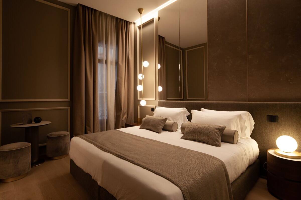 A modern hotel room with a large bed, a vanity with lights, and a mirror.