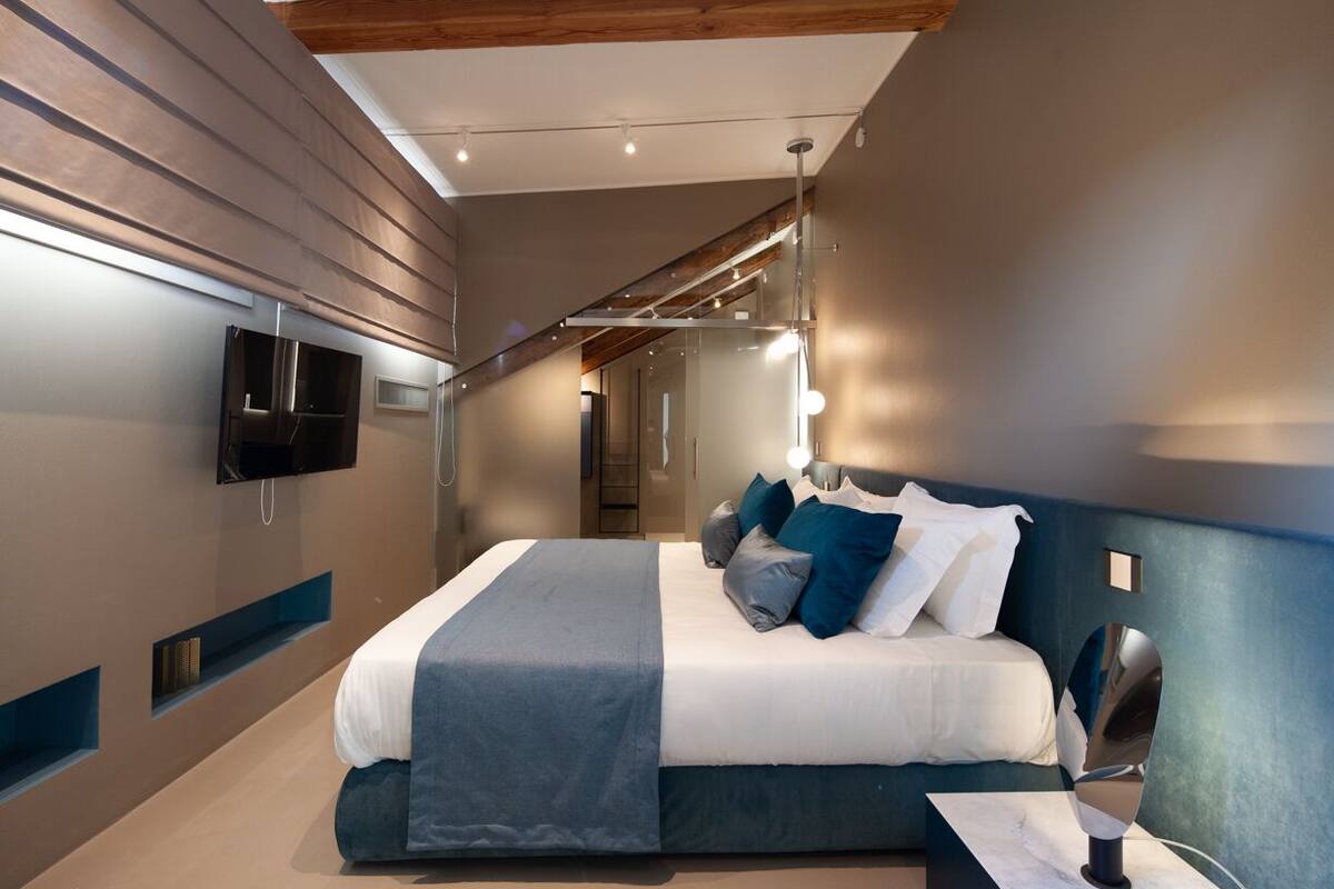 A modern bedroom with a bed, bedside table, and a flat-screen TV mounted on the wall.