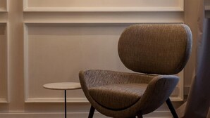 A modern chair with a round back and a small side table, positioned in front of a wall-mounted light fixture with multiple bulbs. - Palazzo Pianca (Venice)