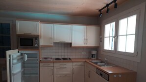 Keittiössä on valkoiset kaapit, mikroaaltouuni, jääkaappi, kahvinkeitin ja pesuallas.