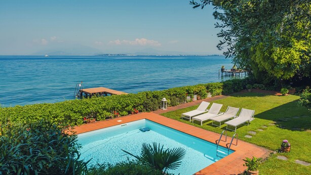 Ein Pool mit Meerblick, umgeben von Gr ünflächen und einer Sonnenterrasse mit Liegestühlen.