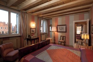 A hotel room with a large bed, a chair, a desk, and a window with curtains. - Domus Nova - Camera Regina Adelaide (Verona)