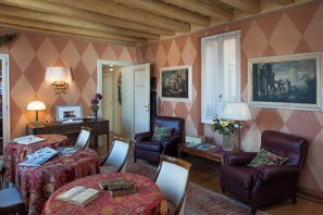 Ein Zimmer mit Holzboden, einem Schreibtisch mit Computer, einem Stuhl, einem Tisch mit einem Buch und einem Gemälde an der Wand.