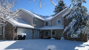 Una casa de dos pisos con techo nevado, entrada y garaje, además de un porche delantero.