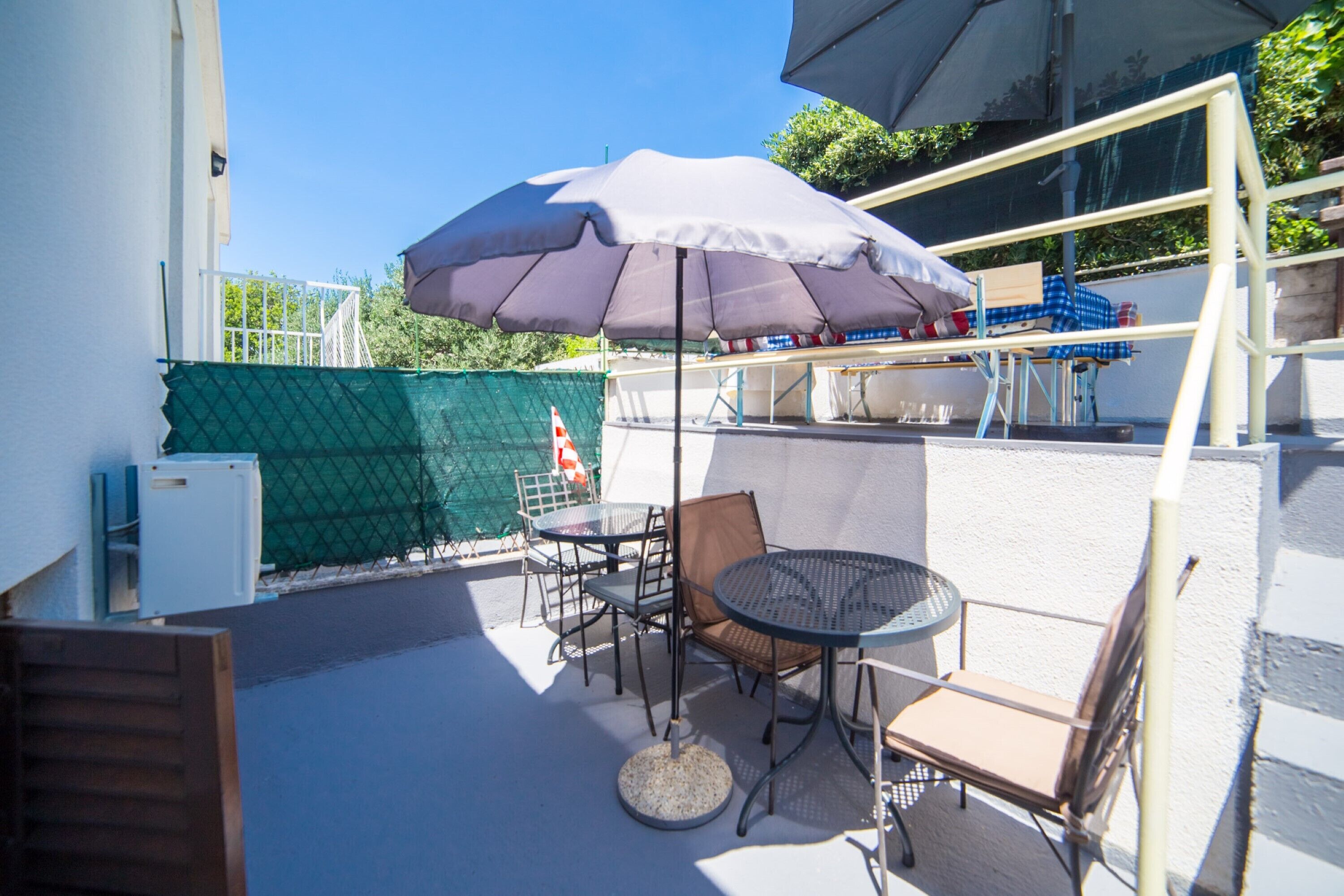 Un patio al aire libre con una mesa, sillas, una sombrilla grande y una valla verde.