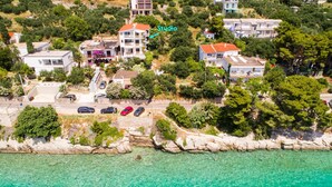 Vue aérienne d’une zone côtière avec des bâtiments, une mer bleue et limpide, et une côte rocheuse.