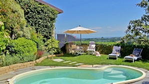 Ein Garten mit Schwimmbad, Liegestühlen und Sonnenschirm.