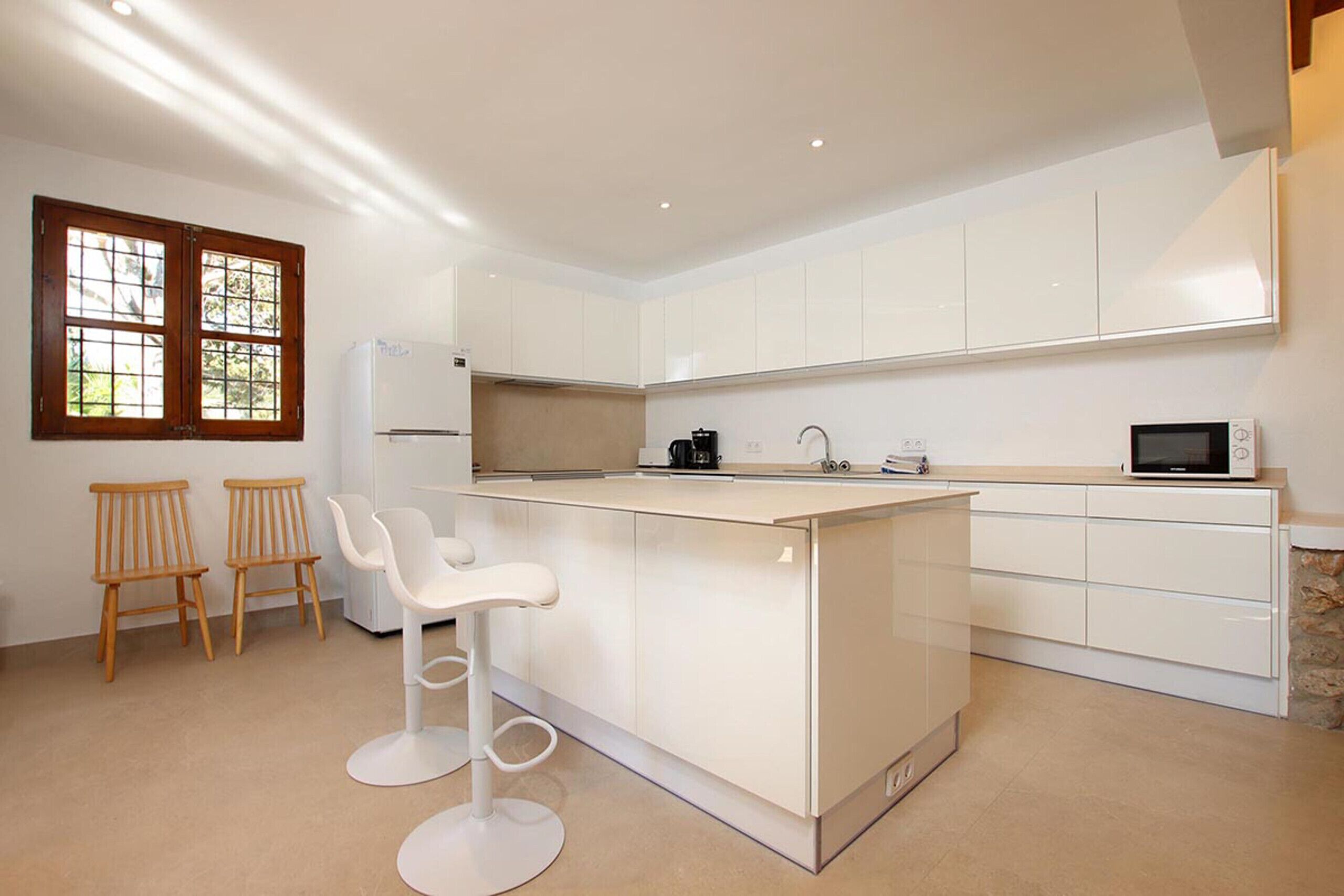 Eine moderne Küche mit weißen Schränken, einer zentralen Kochinsel mit Barhocker, einem Kühlschrank, einer Mikrowelle und einer Kaffeemaschine.