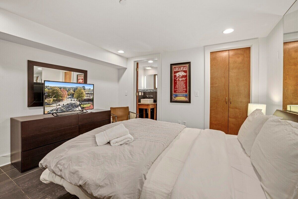 Habitación de hotel moderna con una cama grande, televisor montado en la pared, armario de madera y un cuadro enmarcado de Arkansas.