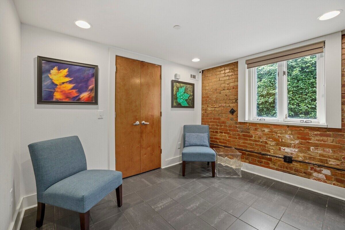 A hallway with two blue chairs, a wooden door, and a brick wall with a window.