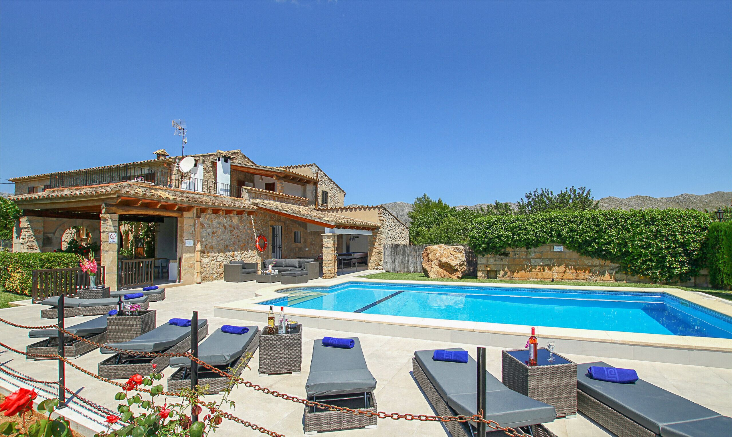 A stone villa with a swimming pool, outdoor seating, and a view of mountains.
