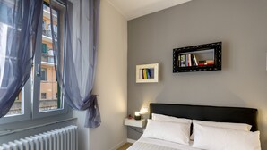 Quarto de hotel com cama, mesa de cabeceira, moldura com imagem e janela com cortinas.