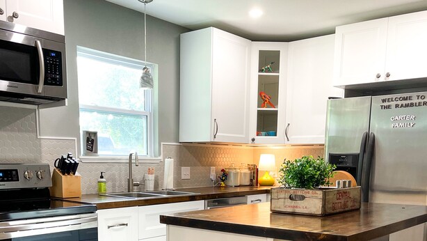 A modern kitchen with white cabinetry, stainless steel appliances, and a central island with bar stools. - Curated for Fun with Hot Tub, Bikes, Fire Pit & More! (Kerrville)