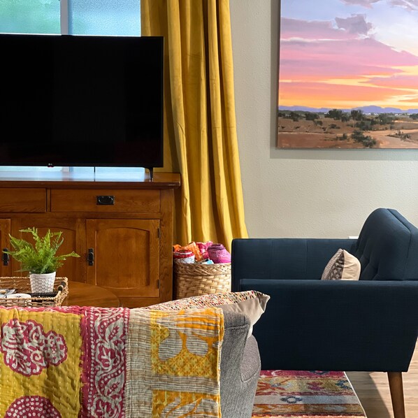 Una sala de estar con televisor de pantalla plana, un sofá azul, un tapete estampado y un cuadro de paisaje.