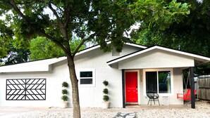 A modern house with a red door, a small porch with a chair, and a paved driveway. - Curated for Fun with Hot Tub, Bikes, Fire Pit & More! (Kerrville)