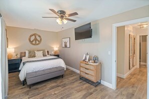 A bedroom with a bed, bedside tables, a ceiling fan, a wall-mounted TV, and a wooden dresser.