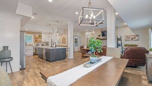 Un vaste espace de vie comprenant un coin repas avec une table en bois, une cuisine dotée d’un îlot central et un coin salon confortable avec une cheminée.