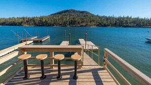 Une jetée en bois, avec une table et des chaises, donnant sur un lac paisible, le tout entouré d’une colline boisée.