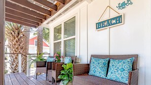 Eine überdachte Veranda mit Korbmöbeln, einem Schild mit der Aufschrift 'BEACH' und einer Palme.