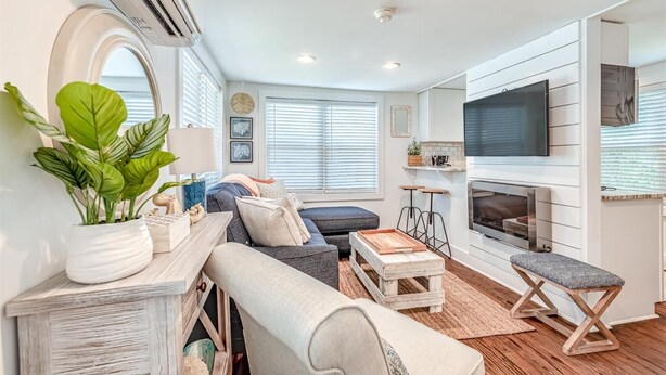 Ein modernes Wohnzimmer mit Sofa, Couchtisch und Kamin. Ein Fernseher ist an der Wand befestigt und eine Zimmerpflanze steht daneben.