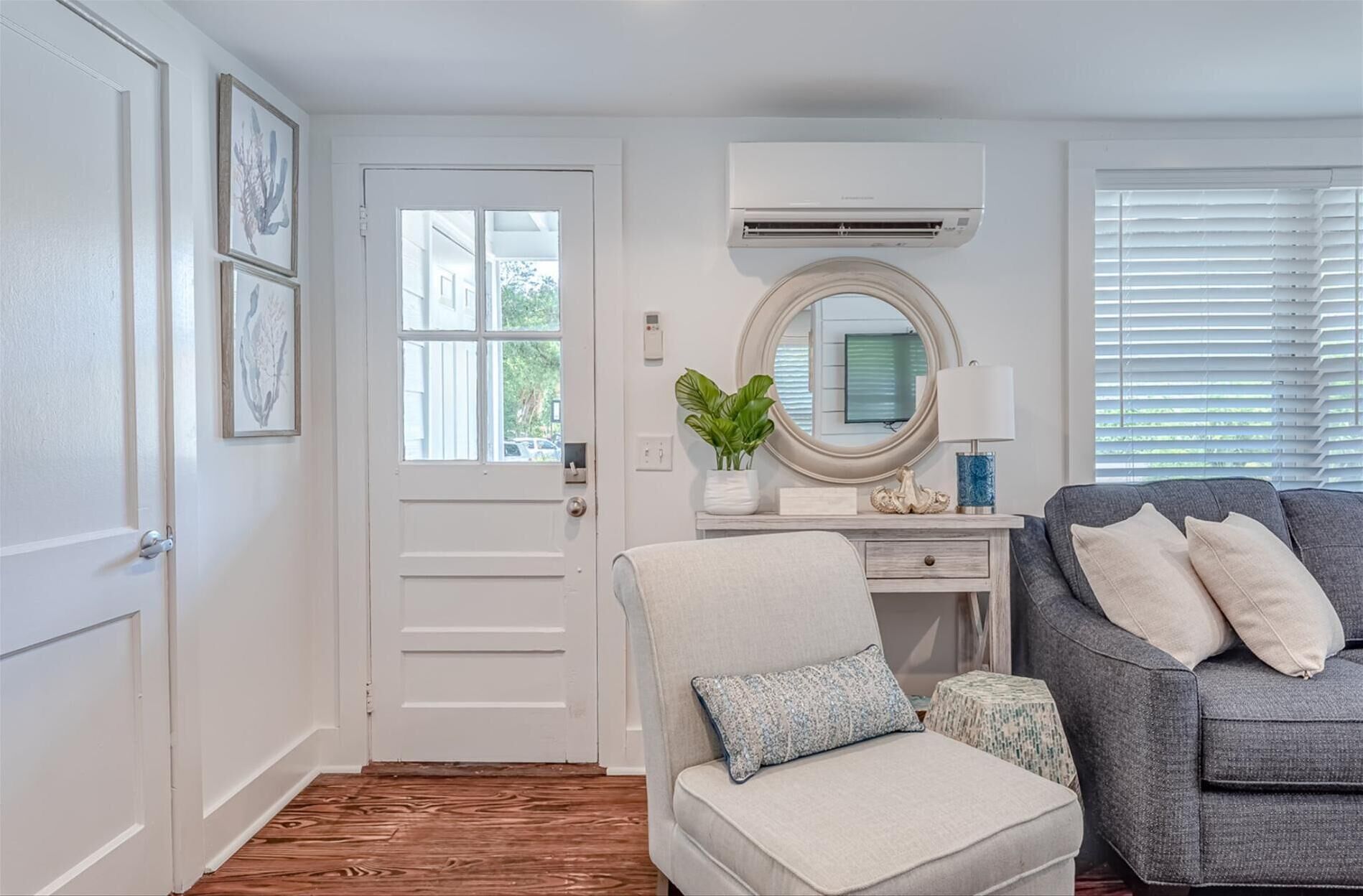 A modern living room with a white door, a grey sofa, a small round table, and a white armchair with a cushion.
