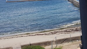 Blick auf die Küste mit Sandstrand, einer Betonmauer und einem Leuchtturm in der Ferne.