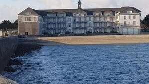 Ein großes, mehrgeschossiges Gebäude mit einem markanten Turm, nahe einem Strand mit steiniger Küste.