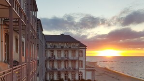 Ein mehrstöckiges Hotel mit Balkonen mit Blick auf einen Strand bei Sonnenuntergang.