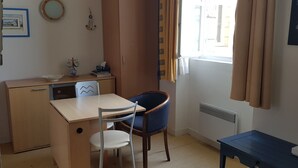 Ein kleiner, gut beleuchteter Raum mit Schreibtisch aus Holz, einem Stuhl, einer Heizung und einem Fenster mit Vorhängen.