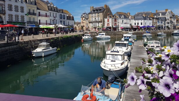 Ein Hafen mit vertäuten Booten, eine Uferpromenade und Gebäude mit Geschäften und Cafés.