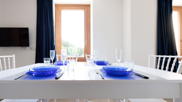 A dining table set with blue glassware and plates, white chairs, and a flat-screen TV mounted on the wall. - Villa Tola - Blu - One Bedroom Apartment, Sleeps 5 (Valdisotto)