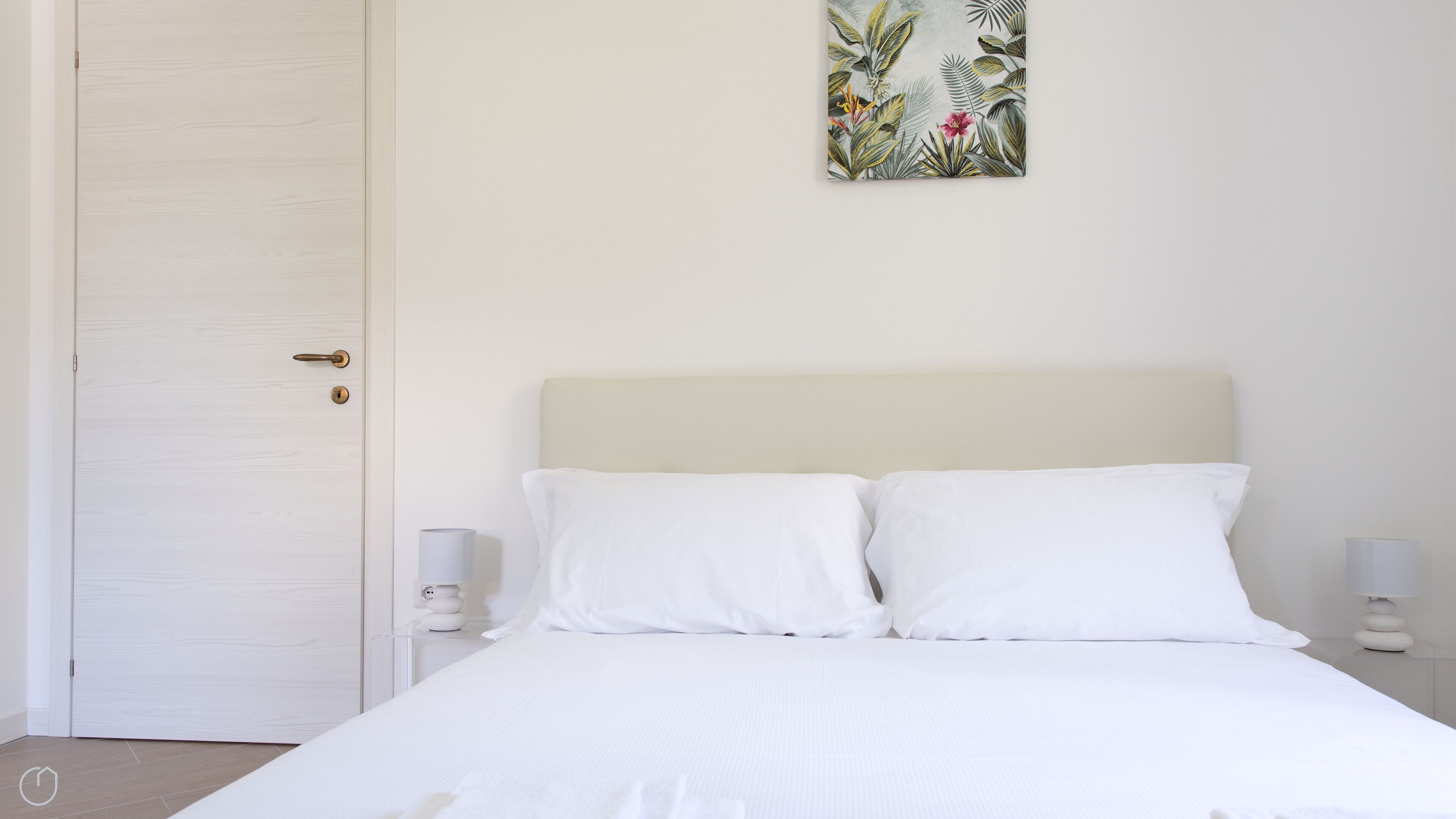 Une chambre à coucher avec un lit, des murs blancs, une porte et une œuvre d’art accrochée au mur.