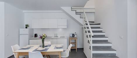 A modern kitchen with white cabinets, a dining area with a table and chairs, and a staircase leading to another level.