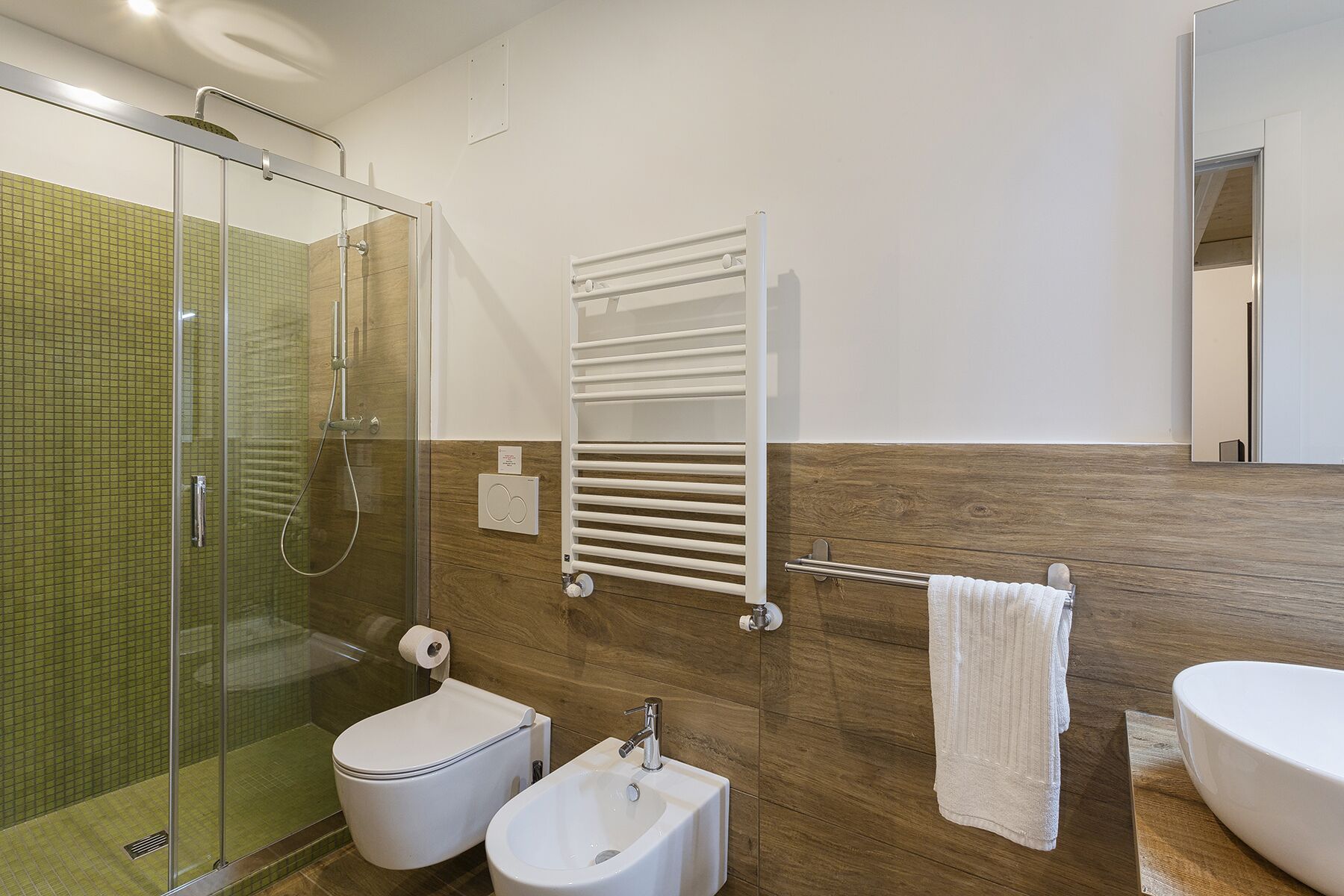 Ein modernes Badezimmer mit Duschkabine aus Glas, Toilette, Bidet, Waschbecken, Handtuchhalter und Spiegel.