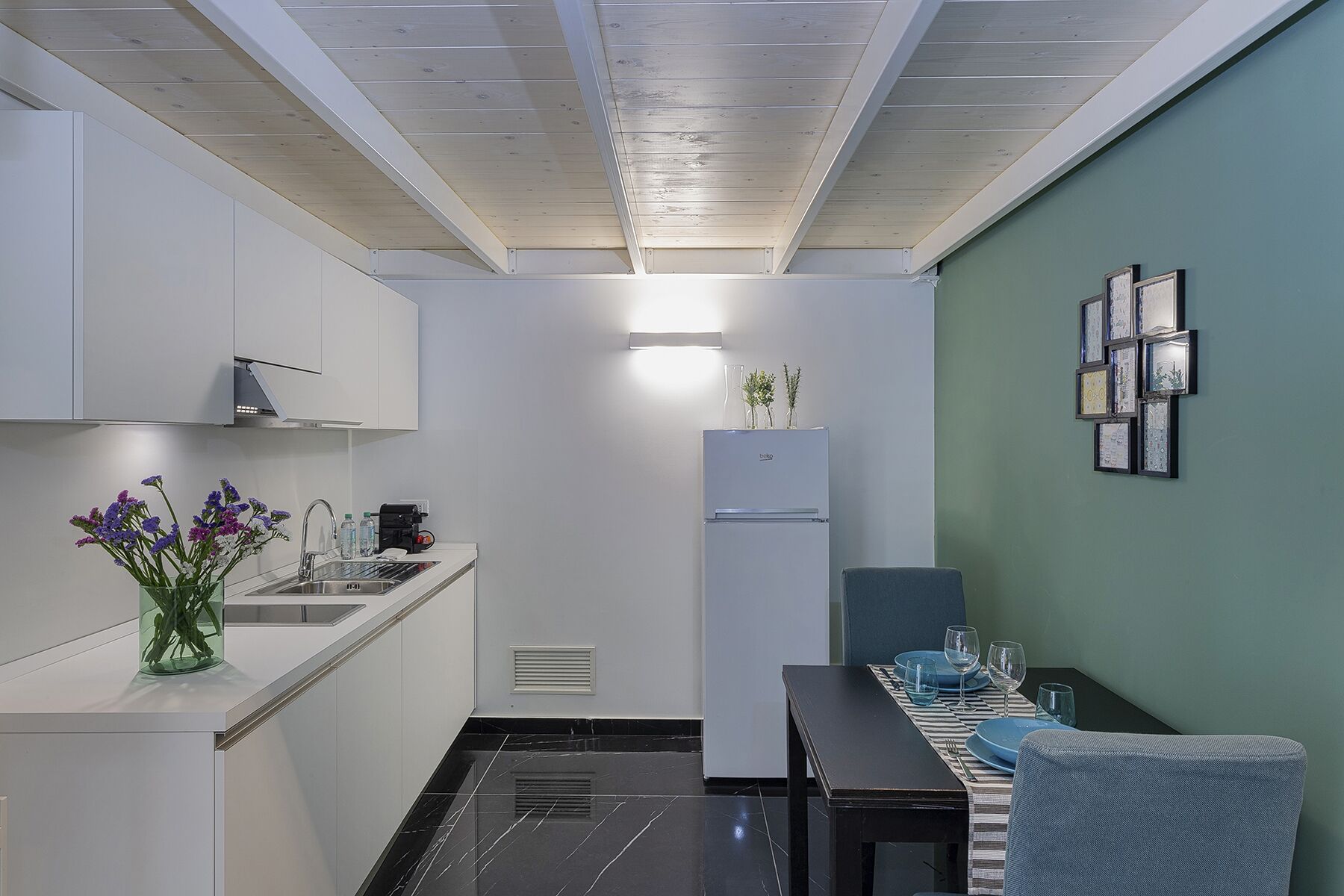 A compact kitchen with white cabinets, a built-in sink, and a dining area with a table set for two.