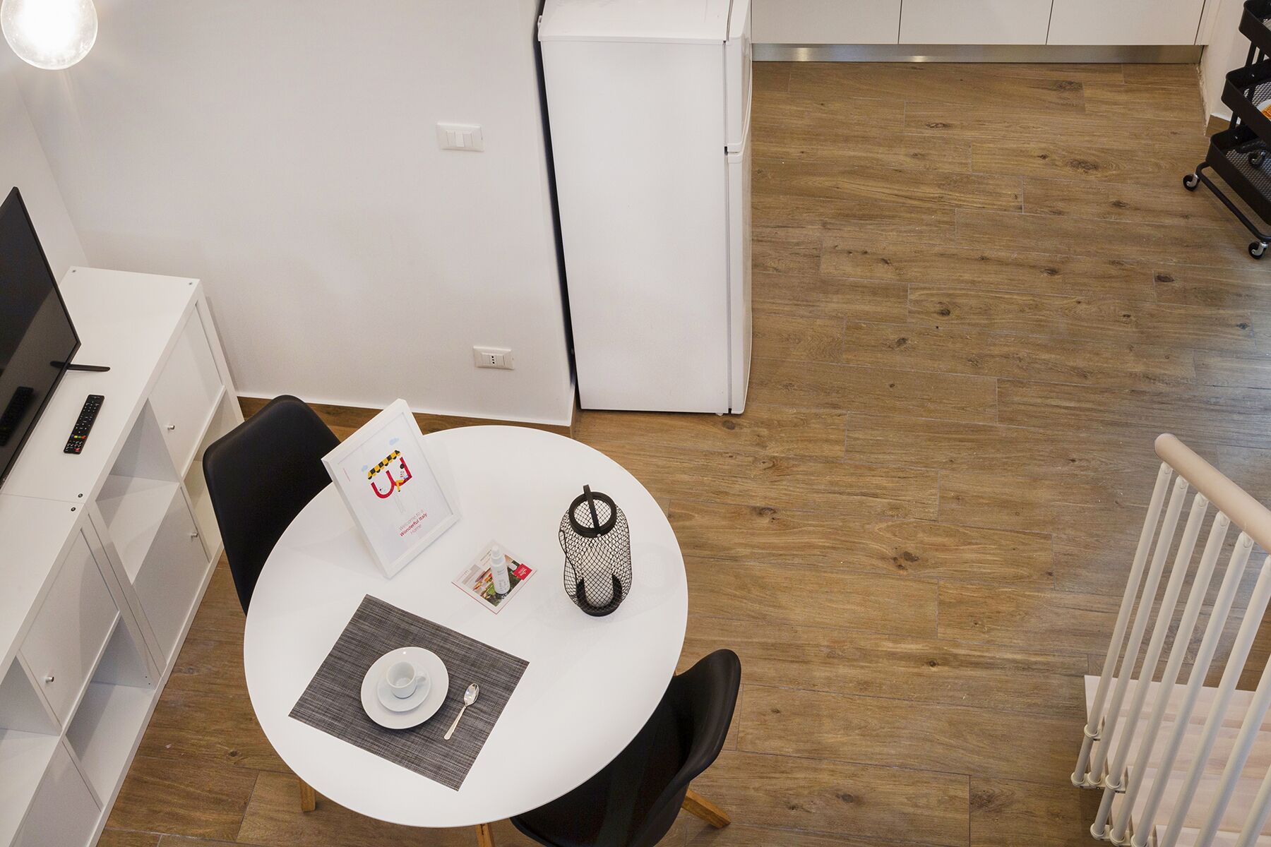 A compact kitchen with white cabinets, a white refrigerator, and a dining area with a round table, black chair, and a placemat.