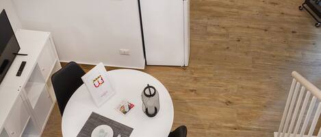 A compact kitchen with white cabinets, a white refrigerator, and a dining area with a round table, black chair, and a placemat.