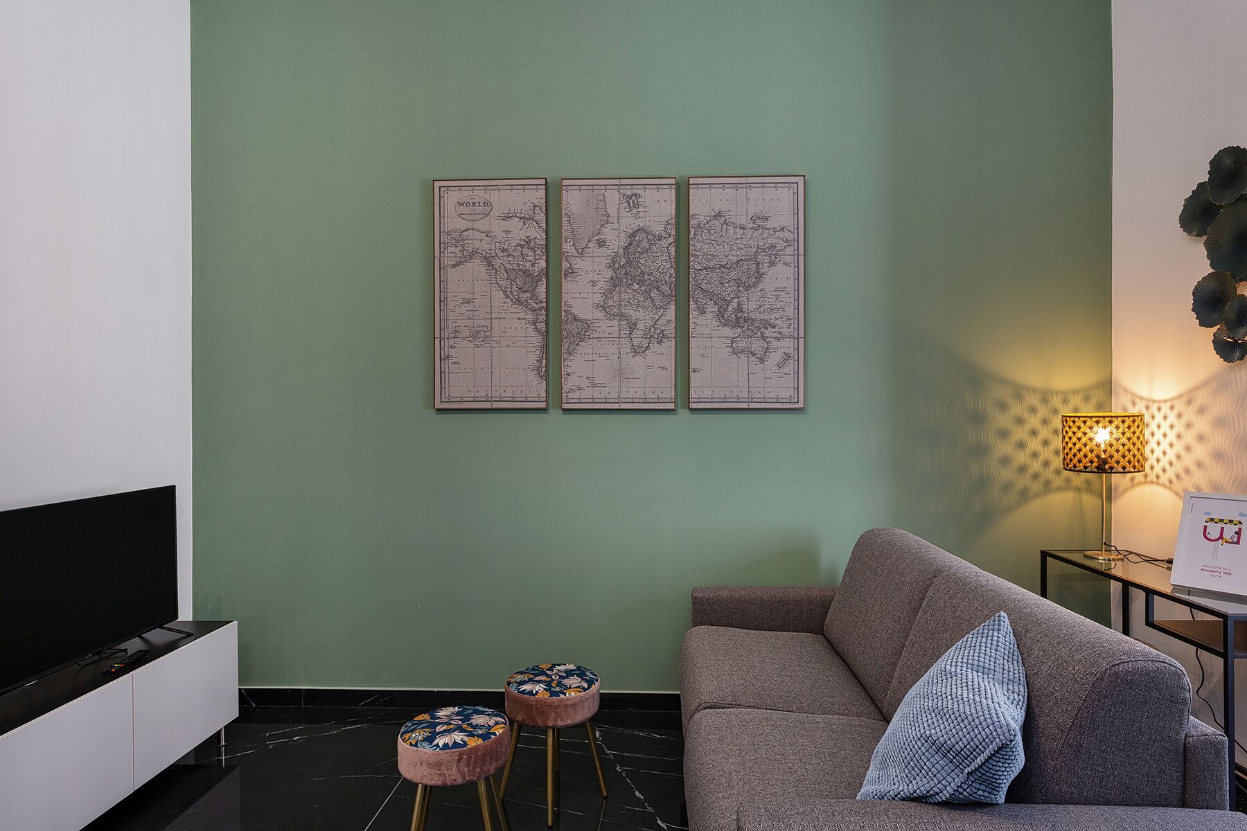 Un salon moderne avec un mur vert, un canapé gris et une petite table ronde agrémentée d’un coussin à motifs floraux.
