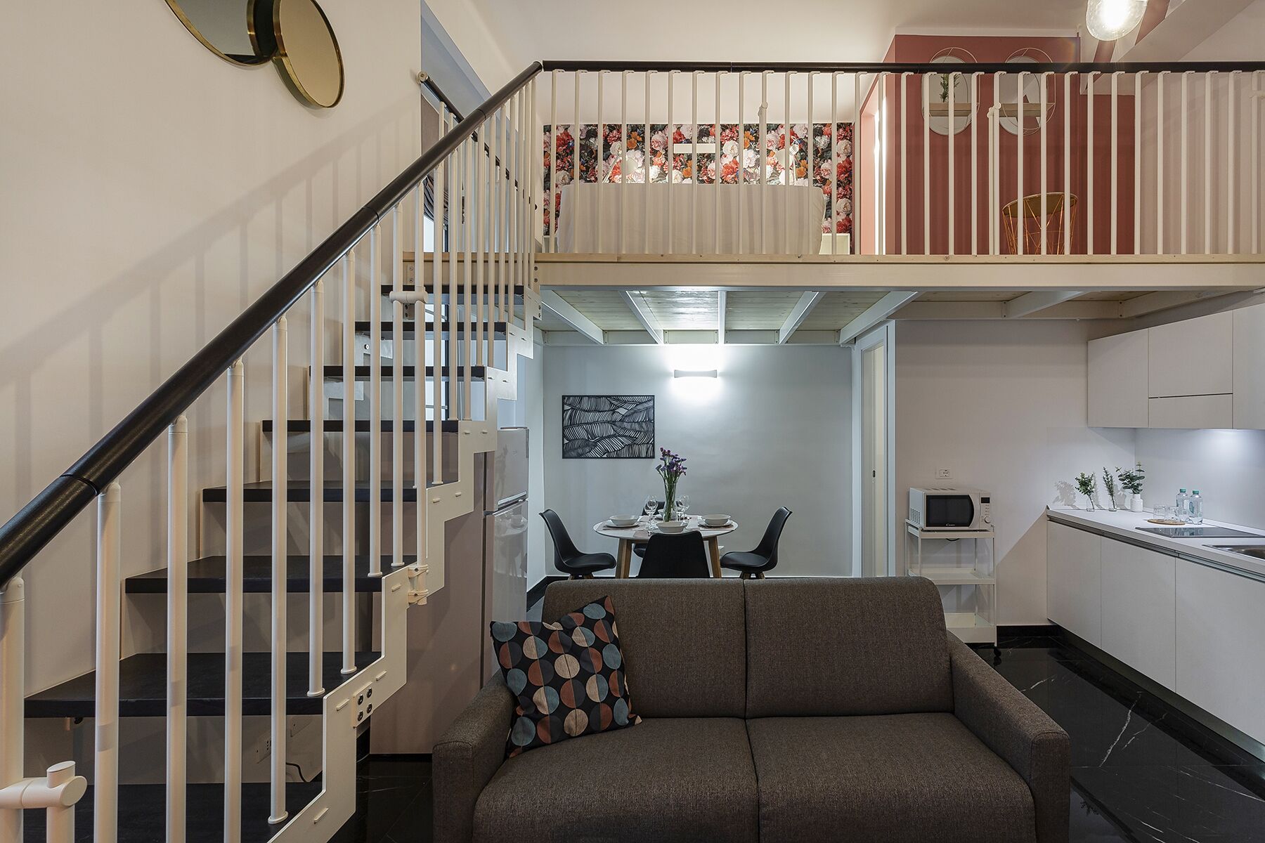 A modern apartment with a staircase leading to a balcony, a dining area, and a kitchen.