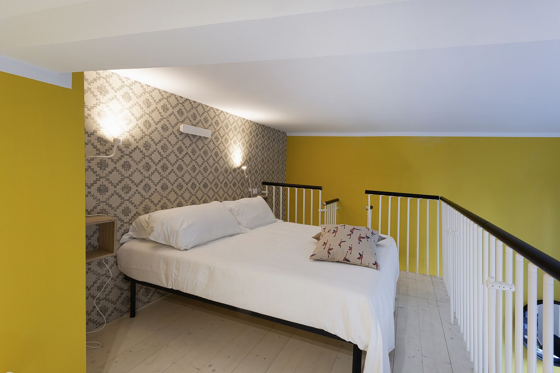 A bedroom with a bed, a nightstand, a patterned wallpaper, and a yellow wall.