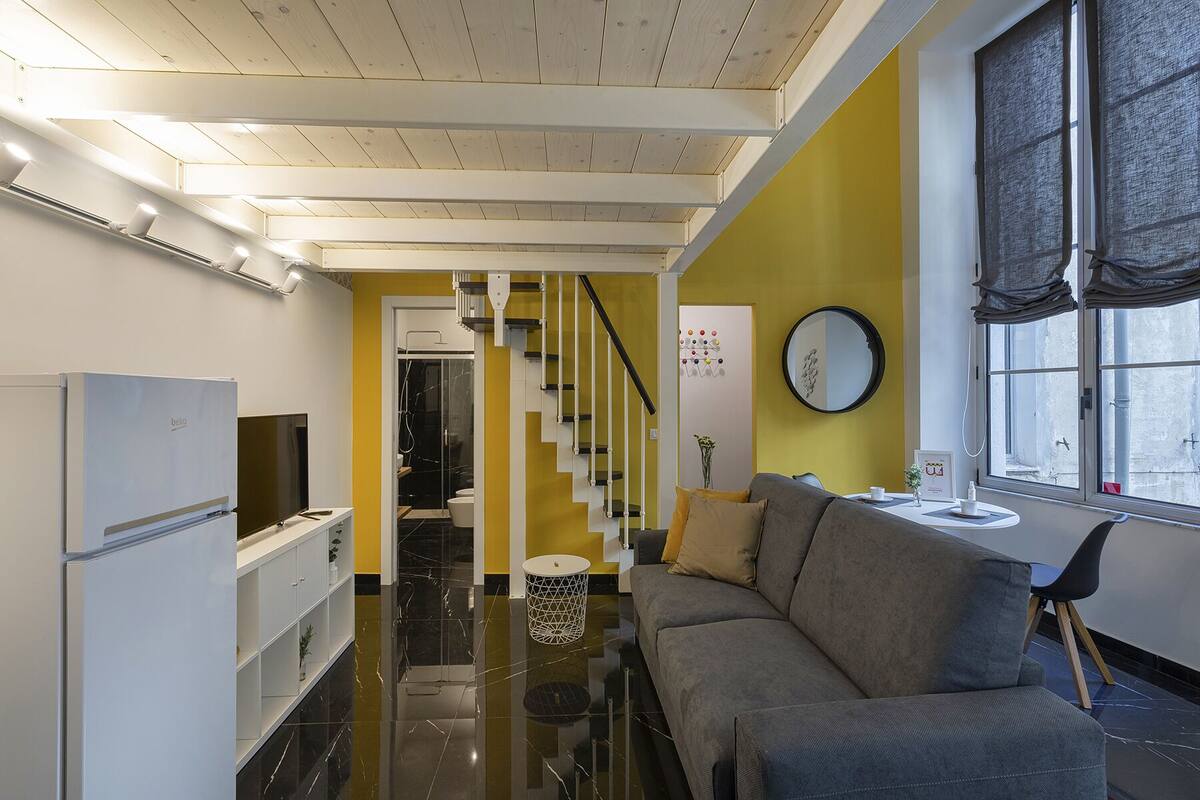 Eine moderne Küche mit Kühlschrank, ein Essbereich mit Sofa und Tisch, eine Treppe zu einem Badezimmer und ein Fenster mit Blick.