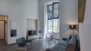 Ett modernt vardagsrum med en tv, en soffa, stolar, ett litet bord och ett stort fönster med gardiner.