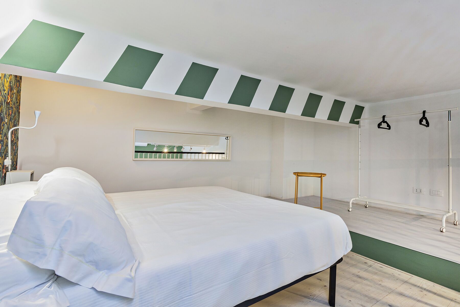 A hotel room with a bed, a small table, a mirror, and a shower area.