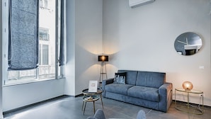 Ett modernt vardagsrum med en grå soffa, en rund spegel och en golvlampa.