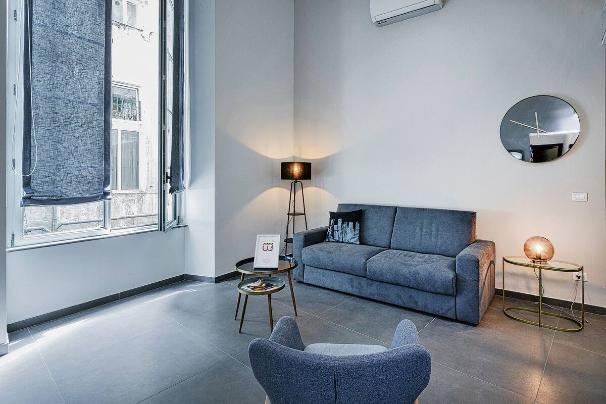 Ein modernes Wohnzimmer mit einem grauen Sofa, einem runden Spiegel und einer Stehlampe.