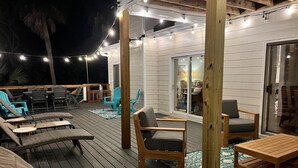Una terraza exterior con mobiliario de madera, incluyendo sillones reclinables y una mesa, y luces colgantes.