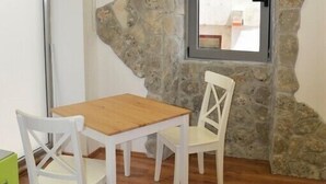 A room with a stone wall, a wooden table, two white chairs, and a window with a view.