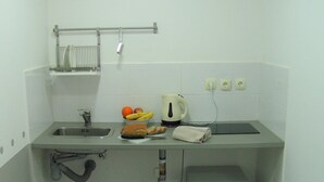 A compact kitchenette with a sink, a kettle, a bread roll, and a fruit bowl.