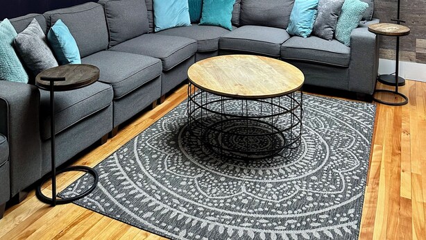 A modern living room with a sectional sofa, a round coffee table, a patterned rug, and a wall mural. - Large 2 Bedroom 1 Bath Apartment right on Main Street in Downtown Ellsworth. (Ellsworth)