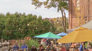 An outdoor seating area with tables and chairs, surrounded by greenery and a brick building. - Large 2 Bedroom 1 Bath Apartment right on Main Street in Downtown Ellsworth. (Ellsworth)